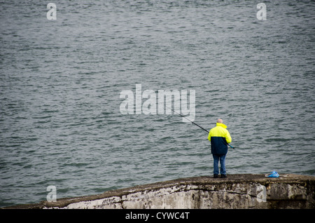 BEAUMARIS, pays de Galles — Un pêcheur solitaire jette sa ligne d'un vieux mur de pierre le long du front de mer de Beaumaris sur l'île d'Anglesey. La scène paisible capture l'attrait intemporel de la pêche à la ligne en mer avec pour toile de fond le détroit de Menai, avec les montagnes de Snowdonia visibles au loin. Cette image résume le charme tranquille et la beauté naturelle qui attirent les pêcheurs et les touristes dans cette pittoresque ville côtière galloise. Banque D'Images