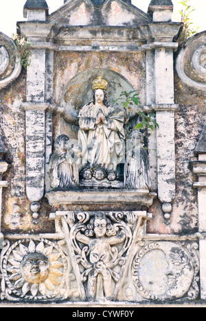 Sculptures d'église Antigua Guatemala // ANTIGUA GUATEMALA, Guatemala — des sculptures complexes ornent l'extérieur d'une église partiellement en ruine. Le relief de pierre détaillé représente des figures religieuses, y compris une figure centrale couronnée avec les mains serrées dans la prière, flanquée d'autres statues. Ci-dessous, des têtes chérubiennes et des éléments décoratifs comme le soleil et la lune sont visibles, tous montrant des signes d'âge et d'altération. Banque D'Images