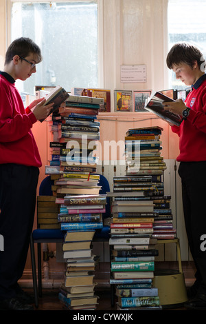 Deux garçons lecture article par une pile de manuels scolaires et de romans dans la bibliothèque d'une école secondaire au Pays de Galles, Royaume-Uni Banque D'Images