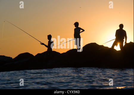 Pêche à trois personnes sur les rochers d'un rivage à la méditerranée en Italie Banque D'Images