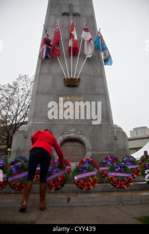 Une femme quitte son coquelicot sur une couronne de fleurs le jour du Souvenir au cénotaphe de Vancouver's Place de la victoire. Banque D'Images