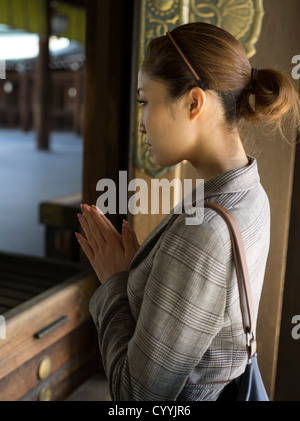 Belle jeune femme japonais visitant Meiji Jingu, Tokyo. Priant au hall principal, shaden, du sanctuaire. Banque D'Images