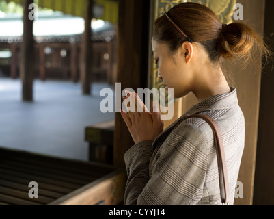 Belle jeune femme japonais visitant Meiji Jingu, Tokyo. Priant au hall principal, shaden, du sanctuaire. Banque D'Images