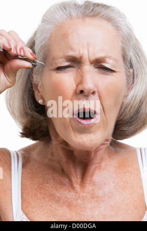 Senior woman tweezing sourcils against white background Banque D'Images