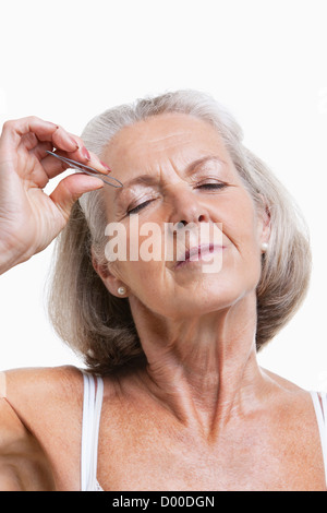 Senior woman tweezing sourcils against white background Banque D'Images