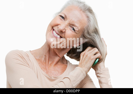 Portrait of smiling senior woman combing her hair against white background Banque D'Images