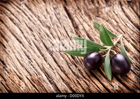 Olives noires mûrs avec des feuilles sur un fond de bois. Banque D'Images
