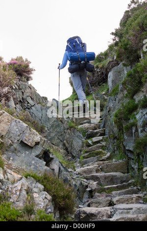Une femme hiker walking up un chemin en pierre avec un grand sac à dos dans le Lake District. Banque D'Images