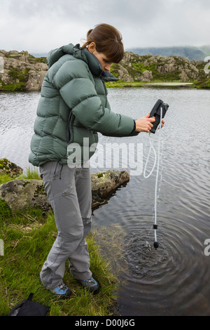 Le filtrage d'une femme de l'eau dans une bouteille en plastique d'une montagne tarn dans le Lake District. Banque D'Images