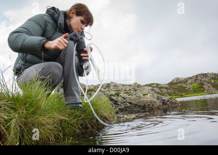 Le filtrage d'une femme de l'eau dans une bouteille en plastique d'une montagne tarn dans le Lake District. Banque D'Images