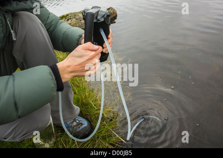 Le filtrage d'une femme de l'eau dans une bouteille en plastique d'une montagne tarn dans le Lake District. Banque D'Images
