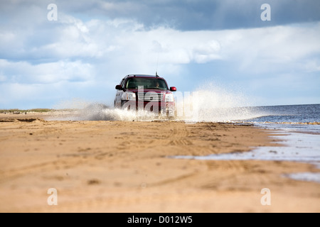 Grande voiture à quatre roues motrices de la conduite sur la côte de la mer de sable dans les projections d'eau Banque D'Images