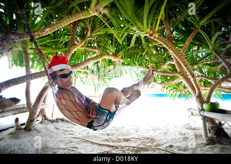 Man in Santa hat in hammock on tropical beach Banque D'Images