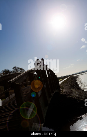 Deux personnes s'appuyant sur la rambarde d'un pont en bois qui se découpent dans la lumière du soleil Banque D'Images