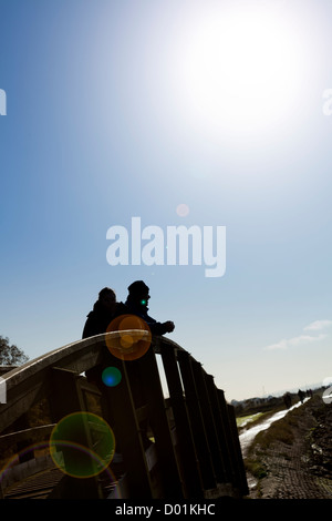 Deux personnes s'appuyant sur la rambarde d'un pont en bois qui se découpent dans la lumière du soleil Banque D'Images