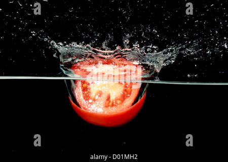 Tranches de tomates dans l'eau avec des bulles d'air sur un fond noir Banque D'Images