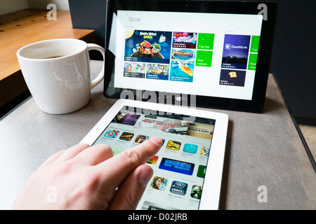 L'homme à l'aide de l'iPad 3 et Microsoft Surface rt tablet computer to browse app stores in cafe Banque D'Images