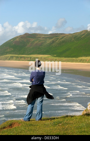 Femme debout en haut d'une falaise, regardant les vagues et la plage, Rhossili bay, la péninsule de Gower, Pays de Galles, Royaume-Uni Banque D'Images