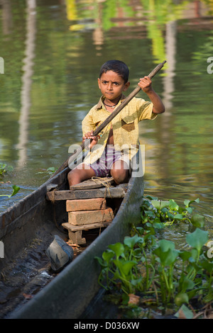 Petit garçon poling un bateau sur une voie navigable à un petit village, près de Kumarakom, Kottayam, Kerala, Inde Banque D'Images