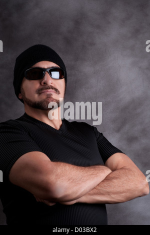 Fier dur en noir. Homme fort en tee shirt noir, lunettes de soleil, et l'ensemencement avec les bras croisés, musculaire Banque D'Images