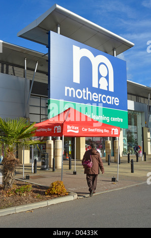 Femme marche vers Mothercare & Early Learning Centre entrée dans grand parc de vente au détail avec Britax siège-auto à l'extérieur de la baie de montage Banque D'Images