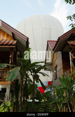 Un ballon à air chaud des terres dans une zone minuscule entre les maisons à Vang Vieng, Laos. Banque D'Images