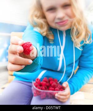 Petite blonde active girl tenue hors de framboises fraîches la totalité de son fort. Portrait en extérieur avec selective focus on berry Banque D'Images