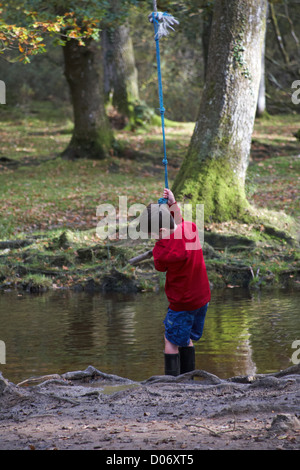 Young boy holding sur corde de pendaison sur arbre à pivoter sur stream à Puttles au Bridge, New Forest en octobre Banque D'Images