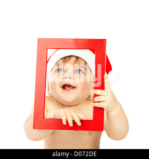 Photo de cute baby boy wearing Santa Claus hat, adorable Enfant tenant cadre rouge dans les mains à la recherche à travers elle, joli petit enfant Banque D'Images