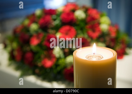 Une bougie brûlante avec un cercueil blanc et un arrangement floral sur l'arrière-plan dans une morgue Banque D'Images