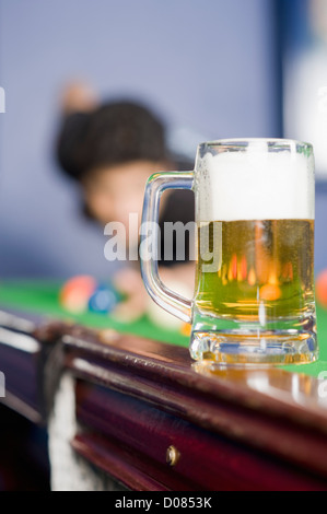 Jeune homme jouant au billard et un verre de bière sur la table de billard Banque D'Images