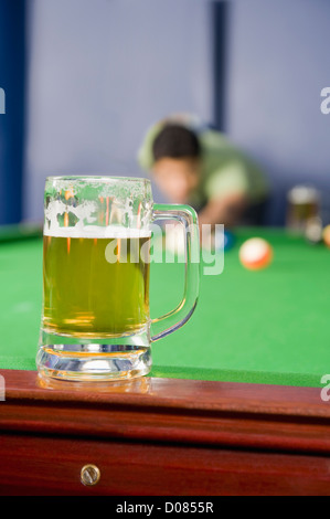 Jeune homme jouant au billard et un verre de bière sur la table de billard Banque D'Images