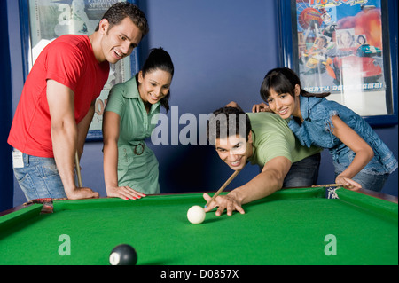 Jeune homme jouant au billard et ses amis à regarder son jeu Banque D'Images