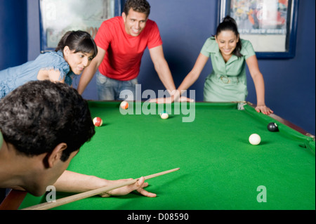 Jeune homme jouant au billard et ses amis à regarder son jeu Banque D'Images