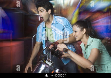 Jeune femme jouant le jeu vidéo et un jeune homme qui regarde son jeu dans une salle de jeux vidéo Banque D'Images