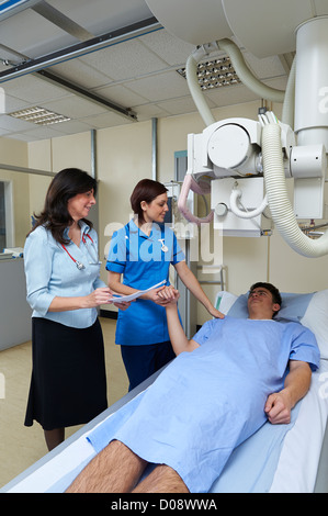 Doctor and nurse talking to patient et rassurant qui est allongé sur une table à rayons X lors de l'enregistrement patient notes Banque D'Images