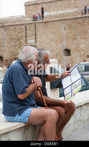 Programme Rallye de Chypre soit lue par deux hommes assis sur un mur à Paphos Chypre Banque D'Images
