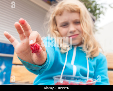 Petite blonde active girl tenue hors de framboises fraîches la totalité de son fort. Portrait en extérieur avec selective focus on berry Banque D'Images