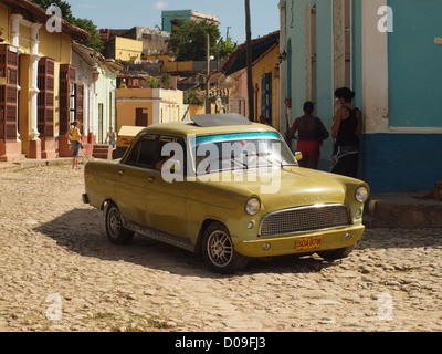 Voiture jaune classique des années 1950 à Trinidad Cuba tournant au coin de la rue Dans une rue pavée cubaine typique Banque D'Images