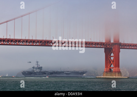 Porte-avions USS Carl Vinson passe lentement sous le golden gate bridge au cours de la semaine de la flotte d'hélicoptères en vol stationnaire en arrière-plan Banque D'Images