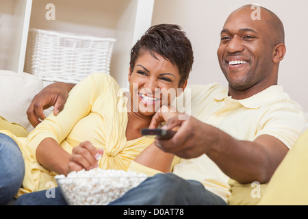 African American couple, homme et femme, s'amusant à regarder la télévision rire et eating popcorn Banque D'Images
