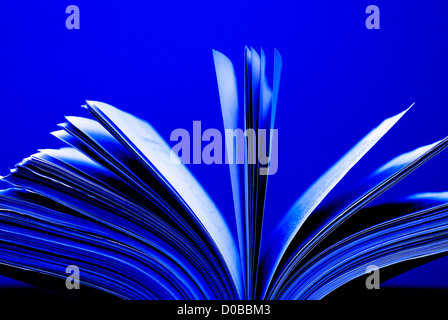 Un grand livre unique assis avec des pages ouvertes sur un bureau et le fond bleu Banque D'Images