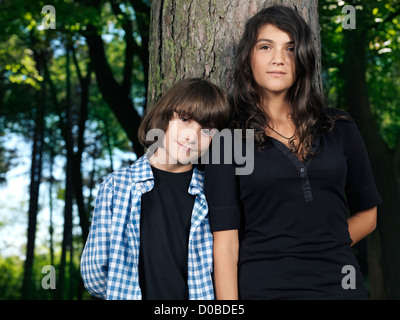 Portrait psychologique d'une jeune soeur et un frère plus jeune, debout appuyé contre un arbre dans la nature