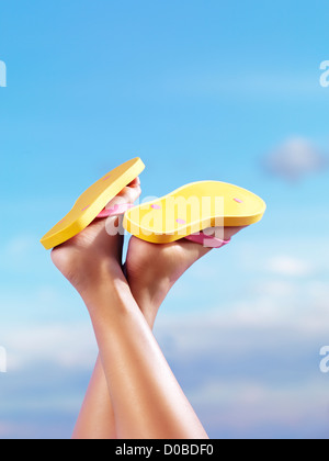 Close up of woman jambes portant des tongs jaune vif sous fond de ciel bleu Banque D'Images
