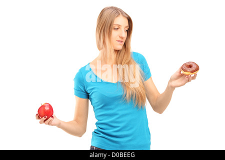 Douteux woman holding an apple and donut essayant de décider lequel de manger Banque D'Images