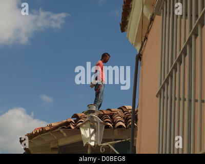 Un constructeur cubain en rouge T-shirt et jeans se dresse au sommet d'un toit pantiled dans la ville UNESCO de Trinidad Cuba Banque D'Images