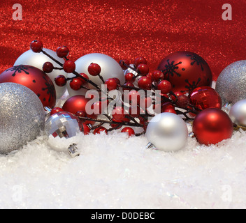 Décorations de Noël niché dans la neige sur un fond rouge cuir Banque D'Images