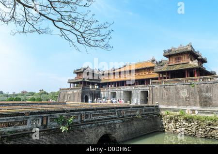 HUE, Vietnam — les touristes traversent le pont sur les douves jusqu'à la porte de la Citadelle à la Cité impériale de Hue, Vietnam. Palais clos et fortifié, le complexe comprend la Cité interdite pourpre, qui était le sanctuaire intérieur de la maison impériale, ainsi que des temples, des cours, des jardins et d'autres bâtiments. Une grande partie de la ville impériale a été endommagée ou détruite pendant la guerre du Vietnam. Il est maintenant classé au patrimoine mondial de l'UNESCO. Banque D'Images