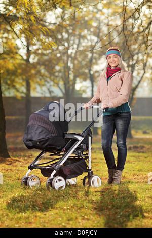 Une mère souriante posant avec une poussette de bébé dans un parc en automne Banque D'Images