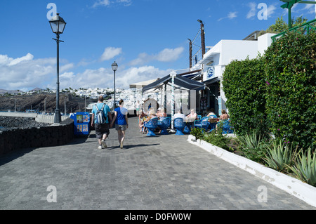 Dh PUERTO DEL CARMEN LANZAROTE Tourist couple walking par outdoor cafe gens assis de détente Banque D'Images